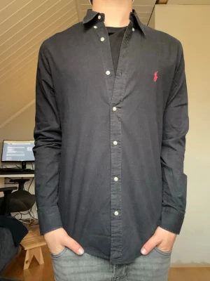 Svart skjorta Ralph lauren skjorta  - Säljer denna Ralph Lauren skjortan i storlek M slim fit. Modellen är 175 väger 65kg och har storlek S. Längd 65cm bredd 48cm armlängd 61cm 