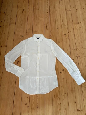 Ralph lauren skjorta  - Säljer en vit skjorta från Ralph lauren. Skjortan är slim fit och är storlek S. Finns tecken på användning men annars i mycket bra skick, 8/10 i skick. Hör gärna av er om ni har några frågor eller funderingar😊