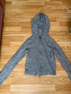 Grå zip-hoodie i mjukt material - En enkel och stilren grå hoodie med dragkedja framtill och huva. Tillverkad i ett mjukt, stickat material som känns skönt mot huden. Långärmad modell med avslappnad passform, lite kort så magen syns lite! perfekt för en chill look. 