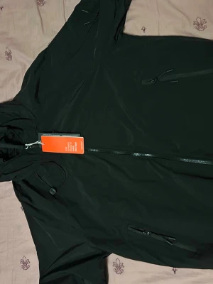 Cp company jacka - Snygg svart vindjacka med huva och dragkedja framtill. Jackan har meshfoder på insidan och en diskret knappdetalj på sidan. Perfekt för blåsiga dagar och enkel att matcha med olika outfits.