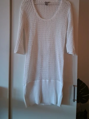 Vit stickad klänning från Filippa K - Vit stickad klänning från Filippa K i 100% bomull. Klänningen har trekvartsärm, rund halsringning och ett genombrutet stickat mönster. Nederdelen är plisserad vilket ger en snygg kontrast till den öppna stickningen.