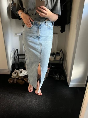Lång jeanskjol med slits framtill - Blå lång jeanskjol i rak modell med hög midja och slits framtill. Jag är 168 cm lång för referens. 