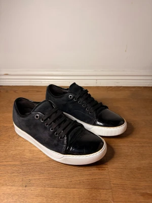 Lanvins - Snygga svarta sneakers med ovandel i mocka och glansiga lackdetaljer på tå och häl. Skorna har svarta skosnören och vit sula som ger en clean kontrast. Perfekta för dig som gillar en stilren men ändå edgy look. Storlek uk 6/ 41 men passar även 42.