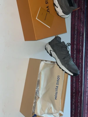 Grå Louis Vuitton sneakers - Säljer ett par gråa Louis Vuitton sneakers med cool mesh- och syntetdetaljer. Skorna har LV-logga på sidan, snörning och en chunky vit och svart sula. Kommer med originalkartong och dustbag. Perfekta för dig som vill ha något exklusivt och trendigt.