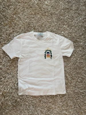 Vit Casablanca tshirt - Säljer en vit t-shirt från Casablanca med färgglatt tryck fram och stort grafiskt tryck på ryggen med texten 'Avenida Casablanca'. Klassisk passform och rund hals. Perfekt för dig som gillar unika prints och streetwear-vibe.