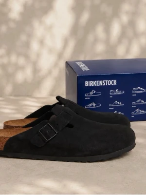 Svarta Birkenstock Boston tofflor - Stilrena svarta Birkenstock Boston tofflor i mocka med justerbart spänne och klassisk korksula. Perfekta för dig som vill ha både komfort och trendig look. Yttersulan har ett mönstrat grepp för extra stabilitet. Obs: ingen kartong