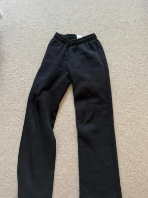 Svarta mjukisbyxor från Gina - Svarta mjukisbyxor från Gina med rak passform och resår i midjan. Tillverkade i mjukt och bekvämt material, perfekta för chill dagar. Klassisk enkel design utan tryck eller detaljer.