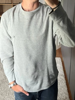 Polo Ralph Lauren - Långärmad Tröja i ljusgrå - stl M - Polo Ralph Lauren våffelstickad långärmad tröja (waffle) i stl M. Skön långärmad i 100% bomull med klassiskt våffelmönster och broderad ponny på bröstet. Tidlös gråmelerad modell, snygg solo eller som lager på skjorta/tröja nu till hösten. Personen på bilden är 189cm, väger 78kg.  Använd men i mycket fint skick, inga hål eller fläckar.  Rök- och djurfritt hem. Skriv gärna om du vill ha fler bilder eller undrar något!