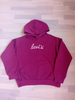 Vinröd hoodie från Levi's med huva - Säljer en vinröd hoodie från Levi's med vit logga på bröstet. Hoodien har stor huva, magficka och ribbade muddar vid ärmslut och nederkant. Perfekt för dig som gillar en avslappnad och snygg stil.