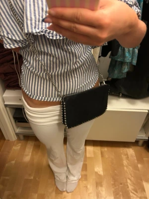 Svart axelväska med kedja - Snygg svart axelväska med silverfärgad kedjerem som man kan ta bort och snygga nitar längst kanterna. Materialet är svart mocka men man kan även se en glittrig nyans. 