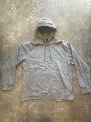 Grå hoodie från SOC med huva - En enkel och clean grå hoodie från SOC i storlek XL. Hoodien har dragsko i huvan, ribbade muddar vid ärmar och nederkant samt en mjuk insida. Perfekt för chill dagar eller när du vill ha något bekvämt och stilrent.