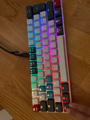 RGB mekaniskt tangentbord 60% - Säljer ett kompakt mekaniskt tangentbord med RGB-belysning. Tangenterna har olika färger och tangentbordet ansluts via USB-kabel. Perfekt för gaming eller skrivande, med snygg design och bakgrundsbelysta knappar i flera färger. Du behöver ha sladd i för att den ska lysa varje gång du trycker ner en talent lyser den 