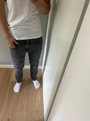 Grå Levis slim fit jeans herr - Säljer ett par sjukt snygga grå slim fit Levis jeans med klassisk femficksdesign och svarta sömmar. Jeansen har normal midja och smal passform hela vägen ner. Perfekta för dig som gillar en modern och enkel stil. Jeansen är W28 men passa upp till W31. Modellen är 179