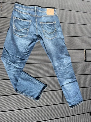 Blå slim fit jeans med slitningar - Snygga blå slim fit jeans med lätt slitna detaljer och klassiska fem fickor. Jeansen har kontrastsömmar och en patch bak i midjan. Perfekta för en avslappnad och trendig look. Materialet är denim i bomull.