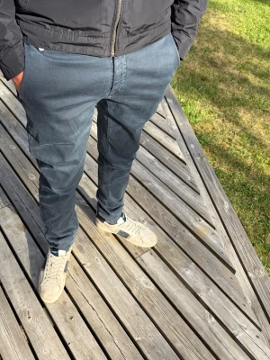 Mörkblå slim fit chinos från Replay - Snygga mörkblå chinos i slim fit-modell med klassisk design och raka ben. Byxorna har diskreta fickor fram och bak, och är tillverkade i ett mjukt och bekvämt bomullsmaterial med lite stretch för extra komfort.