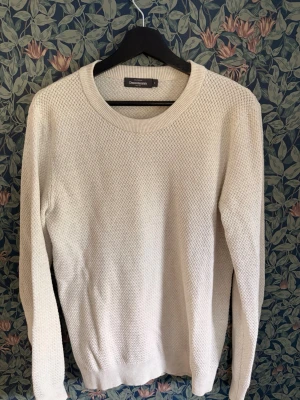 Beige stickad tröja Dressmann - Klassisk vit stickad tröja från Dressmann i storleken S, med rund halsringning och diskret strukturmönster. Tröjan har långa ärmar och ribbade muddar vid ärmslut. Jag på sista bilden är 180cm. Skriv vid minsta fundering.