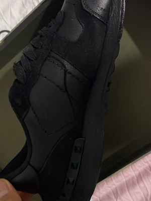 Helvita svarta sneakers med nitar - Säljer ett par helsvarta sneakers med coola nitar på sulan. Skorna har en mix av läder och mocka, samt klassisk snörning. Snygg och stilren design som passar till det mesta. Perfekta för dig som gillar en clean look.