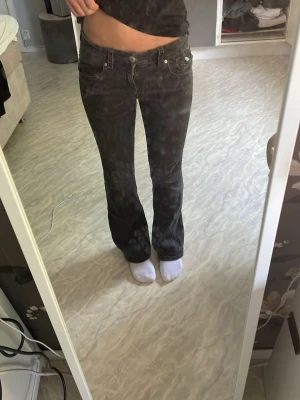 Svarta bootcut jeans med låg midja - Säljer ett par svarta bootcut jeans med låg midja och klassiska fem fickor. Jeansen har en snygg passform och silverfärgade detaljer på fickorna. Perfekta för dig som gillar en avslappnad men trendig stil.