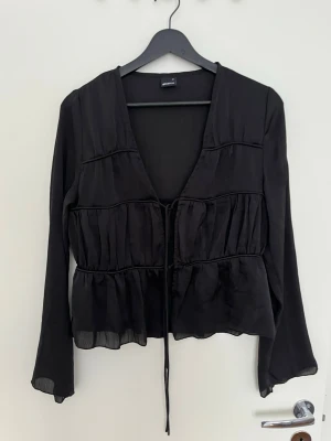 Svart blus från Gina Tricot - Säljer en snygg svart blus med två knytband framtill. Den har en superfin passform och långa ärmar som är lite utsvänga. Perfekt för både vardag och speciellare tillfällen