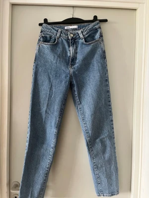 Mum fit jeans från ZARA - Säljer ett par klassiska blå  jeans från ZARA i storlek 34. Jeansen har hög midja, fem fickor och stängs med knapp och dragkedja. Tillverkade i slitstark denim med kontrastsömmar. Perfekta för en avslappnad och trendig look.