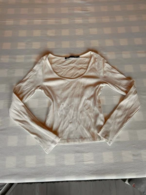 Vit ribbad långärmad topp - (Sitter som en storlek S)Snygg vit ribbad topp med lång ärm och rundad urringning. Modellen har en tight passform som framhäver figuren. Perfekt att styla med jeans eller kjol för en trendig look.