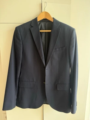 Mörkblå kavaj - Stilren mörkblå kavaj i storlek 46 från HM. Kavajen kommer precis från kemtvätt och är använd ett fåtal gånger. Perfekt för en dressad look och passar till skjorta eller t-shirt.