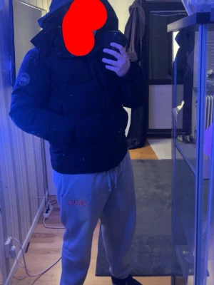 Canada goose vinterjacka  - Säljer en svart dunjacka från Canada Goose med huva och diskret logotyp på ärmen. Jackan har en klassisk puffer-modell med dragkedja och knappar framtill samt två sidofickor dragkedjan för att stånga jackan har åkt av har tappat den ute så den kan man köpa ny sen har den ett hål i vänster armhåla pris går att diskutera