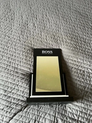 Svart sminkspegel från Hugo Boss - Stilren sminkspegel från Hugo Boss i svart med rektangulär form och stabil fot. Spegeln har en modern design med vit logga upptill och passar perfekt på sminkbordet. Tillverkad i glas och plast för en lyxig känsla.