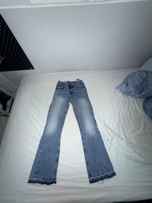 Blå flared jeans med rå kant - Säljer ett par blå flared jeans med slitningar och råa kanter längst ner. Jeansen har en klassisk femficksmodell och är tillverkade i denim. Perfekta för dig som gillar en avslappnad och trendig stil. Varan har använts 1 gång. Storleken är ungefär mellan w29-w30. 
