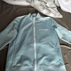 Ljusblå tracksuit  från Palm Angels - Säljer en stilren ljusblå tracksuit från Palm Angels i storlek M-L den är använd men i bra skick, skriv om ni har frågor kring storlek eller annat 😁 kan även byta mot andra tracksuits 