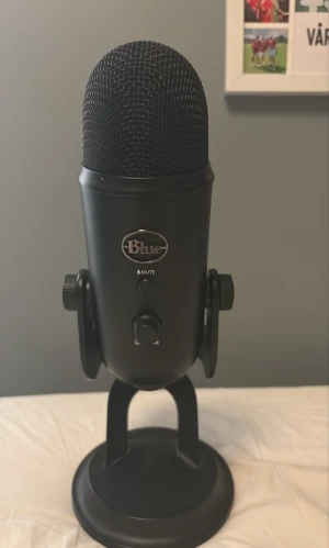 Svart Blue Yeti USB-mikrofon - Säljer en svart Blue Yeti USB-mikrofon med robust metallstativ. Mikrofonen har flera reglage för ljudinställningar och mute-knapp på framsidan. Perfekt för streaming, podcast eller gaming. Klassisk cylinderformad design med metallgaller upptill.