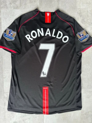 Manchester United Ronaldo fotbollströja - Helt ny svart Manchester United matchtröja med Ronaldo och nummer 7 på ryggen. Perfekta  fotbollströjan om du älskar Ronaldo, ännu bättre om du gillar färgen svart. Passar även dig som har storlek M 