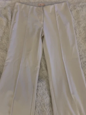 Vita kostymbyxor från Nelly låg midja+ bootcut - Säljer ett par stilrena vita kostymbyxor från Nelly. Byxorna har utsvängda ben, pressveck framtill och låg midja. Materialet känns mjukt och har en lätt glans. Perfekta för en clean och trendig look.