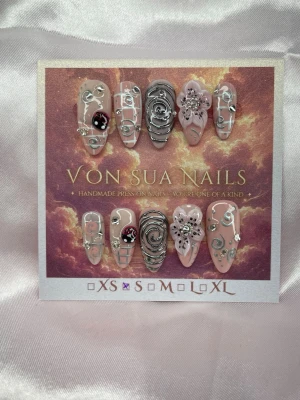 Élan (S);Medium Almond - Unika handgjorda press-on naglar i nude och rosa med silverdetaljer, 3D-blommor och swirlmönster. Några naglar har en nyckelpiga 🐞 samt silver 3D nail art. Medium långa och i en almondform för en whimisical look. Perfekt för dig som vill sticka ut med coola detaljer.S: 15 mm, 11,5 mm, 12 mm, 11 mm, 9 mm 