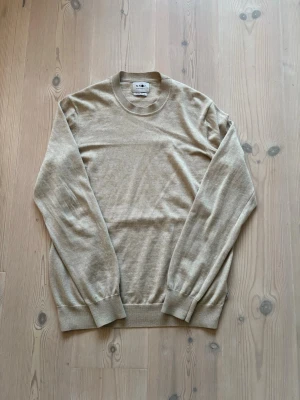 Stickad tröja - En stilren beige stickad tröja med rund halsringning och långa ärmar. Tröjan har ribbade muddar vid ärmslut och nederkant. Perfekt för lager på lager och enkel att matcha med olika outfits.