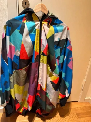 MAXJENNY art fashion and style jacka - Säljer en unik vindjacka från maxjenny med färgstarkt geometriskt mönster i blått, rött, gult, svart, vitt och lila. Jackan har dragkedja framtill och krage. Storlek S/M. Fint begagnat skick utan fläckar eller hål. Ett ovanligt plagg som inte längre säljs. Skicka gärna prisförlag!