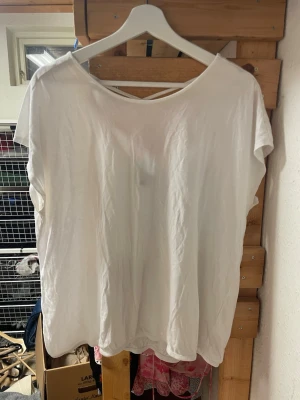 Vit lös topp med criss-cross rygg - Säljer en vit, lös topp i mjuk bomull med korta ärmar och snygg criss-cross detalj i ryggen. Perfekt till jeans eller kjol för en chill och enkel look.
