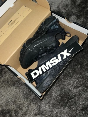 Svarta Nike D/MS/X sneakers - Säljer ett par helsvarta Nike D/MS/X sneakers med cool, chunky sula och meshdetaljer. Skorna har svarta skosnören, diskret swoosh-logga på sidan och dragflik bak. Perfekta för dig som gillar streetwear och sportig stil.