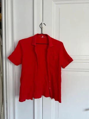 Brand unknown - Röd kortärmad skjorta - Snygg röd skjorta med korta ärmar och klassisk krage. Skjortan har en bröstficka och knappar framtill. Perfekt för dig som vill sticka ut med färg i din outfit.