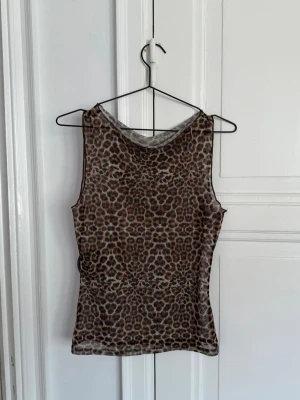 Missguided - Leopardmönstrad ärmlös mesh-topp - Säljer en snygg ärmlös topp i mesh med leopardmönster. Toppen har en tight passform och är perfekt för dig som vill sticka ut med ett djurmönster. Materialet är tunt och lätt, vilket gör den skön att bära under varma dagar.
