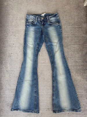 Blå utsvängda jeans - Blå jeans från Gina Tricot i storlek XS med ett vitt streck längs mitten, liknande Cheap Monday-modellen. Innerbenslängd cirka 78 cm och midjemått cirka 34 cm mätt rakt över.