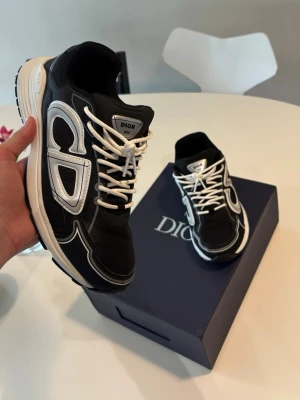 Svarta CD sneakers med vit detalj - Snygga svarta sneakers från CD med vita detaljer och logga på sidan. Skorna har vita snören och en tjock vit sula som ger en sportig vibe. Ovandelen är i mesh och läder för både stil och komfort. Perfekta för dig som vill sticka ut med exklusiva sneakers.