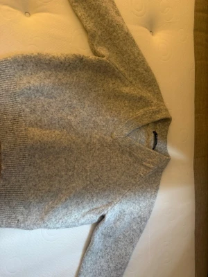 Ljusgrå stickad tröja FB Sister - Mysig ljusgrå stickad tröja från FB Sister med v-ringad hals och ribbade muddar vid ärmslut och nederkant. Perfekt för lager på lager och enkel att matcha till olika outfits. Tillverkad i mjukt material som känns skönt mot huden.