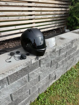 Svart integralhjälm med intercom - Säljer en svart integralhjälm med visir och tillhörande intercom-system. Hjälmen har en slimmad design och ett extra genomskinligt visir medföljer. Intercom-systemet inkluderar mikrofon och högtalare för kommunikation under körning.