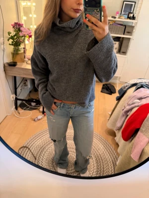 Grå stickad polotröja - Mysig grå stickad polotröja med lös passform och långa ärmar. Tröjan har en hög, vikt krage och är perfekt för kyliga dagar. Materialet ser ut att vara mjukt och bekvämt, vilket gör den enkel att styla till jeans eller kjol.
