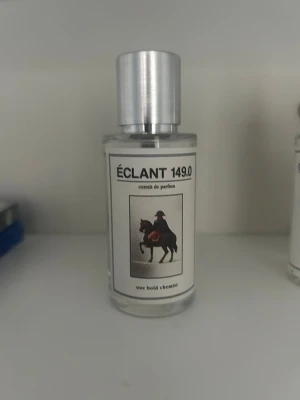 One bold chemist Éclant 149.0 parfymflaska - Stilren parfymflaska med silverfärgat lock och transparent glas. Etiketten har texten ÉCLANT 149.0 och en bild på en ryttare till häst. Flaskan har minimalistisk design och modern känsla, perfekt för dig som gillar unika dofter.