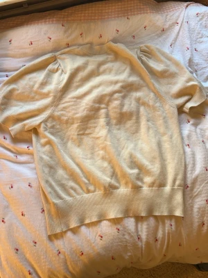Gul topp med puffärm och rosa text - Säljer en ljusgul topp med korta puffärmar och ribbade kanter. På bröstet står det 'AMOUR' i stora, fluffiga rosa bokstäver. Perfekt för dig som gillar söta detaljer och vill sticka ut lite extra.