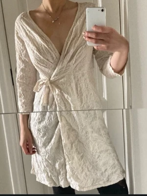  Cottage core, bohemian Odd Molly  dress (M) - Säljer en krämvit omlottklänning från Odd Molly med vackert broderat mönster och knytband i midjan. Klänningen har 3/4-ärmar och djup v-ringning. Materialet är strukturerat och ger en unik look. Perfekt för dig som gillar bohemisk och romantisk stil.