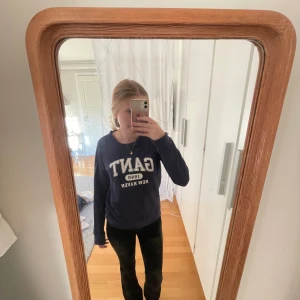 Mörkblå GANT sweatshirt med tryck - Mörkblå sweatshirt från GANT med stort vitt tryck framtill där det står 'GANT 1949 NEW HAVEN'. Tröjan har rund hals, långa ärmar och är gjord i mjuk bomull. Perfekt för en chill och sportig look.