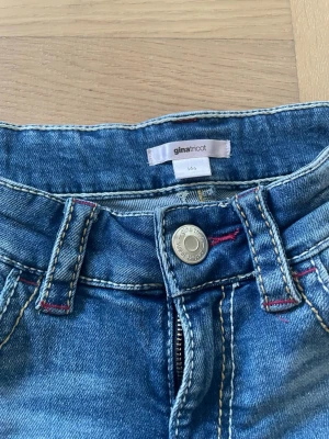 Snygga bootcut jeans - Superfina blå, lågmidjade bootcutjeans från Gina Tricot i strl 164! De är i bra skick utan slitningar och fläckar förutom att trådarna som ska sitta över hålen vid knäna har gått av på ena sidan och istället hänger🫰🏻 Säljer pga att de är lite för korta och baggy för min smak. Hör av dig vid frågor!🥰
